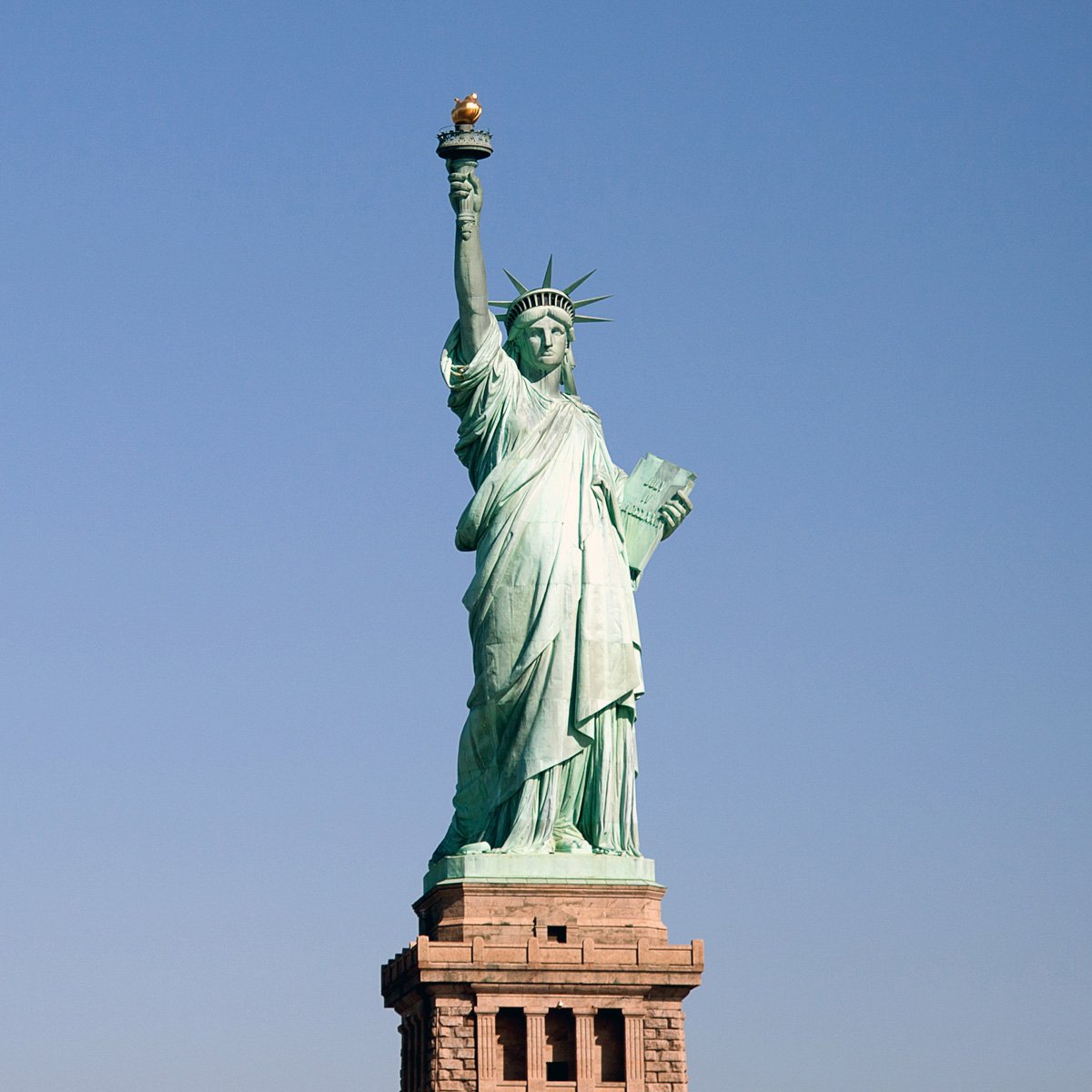 Statue of Liberty holding a torch in her right hand, with a crown on her head, standing on a pedestal against a clear blue sky.
