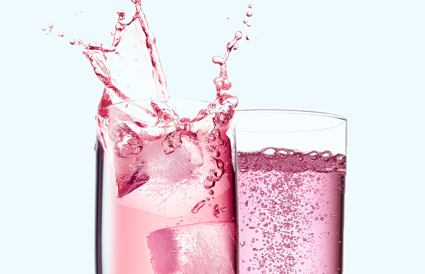 Two glasses of pink liquid, one with ice cubes and splash, on a light background.