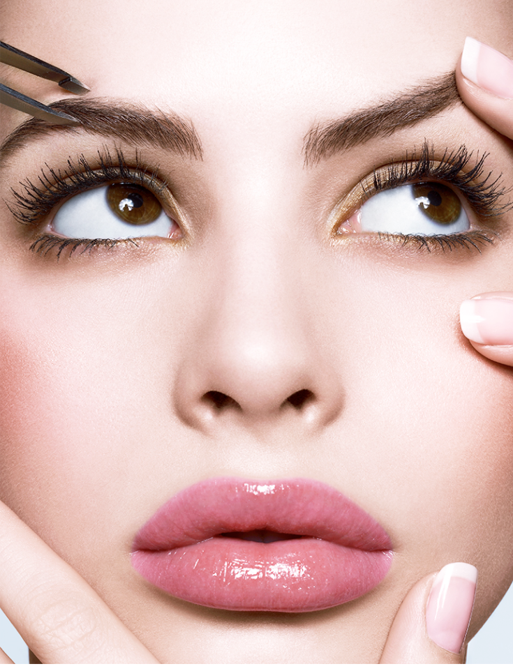 Close-up of a woman's face with makeup, focusing on her eyes, lips, and eyebrows, as someone uses tweezers near her eyebrow.