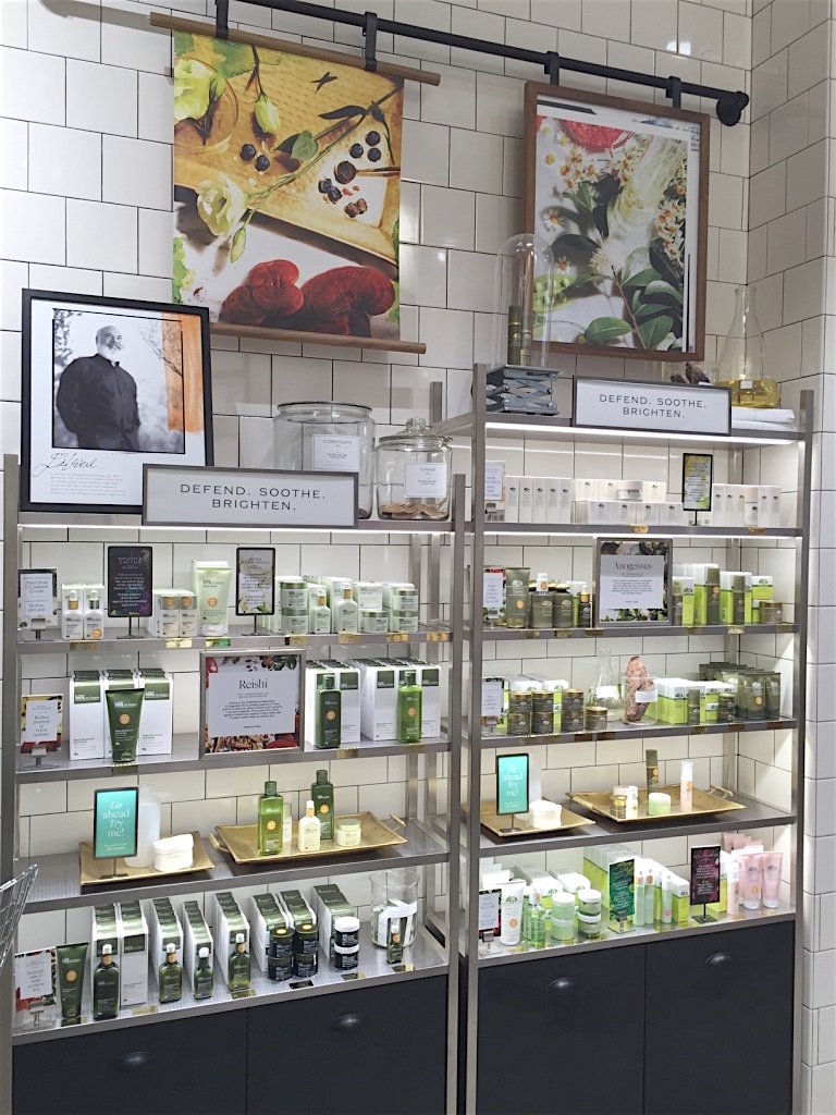 Display of skincare or cosmetic products on shelves in a store, with framed artwork and signs reading 'Defend. Soothe. Brighten.'