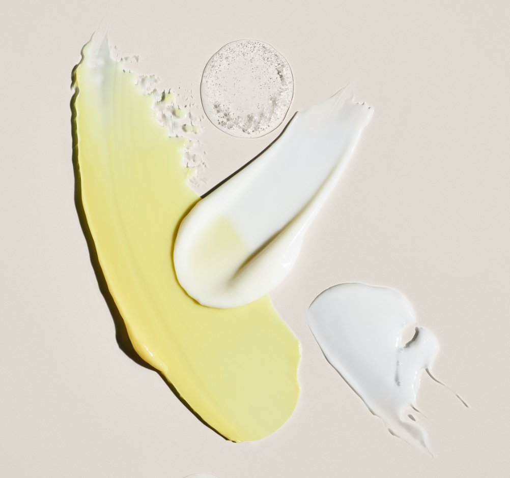 Close-up of various skincare creams and gels in different textures and colors on a light background.