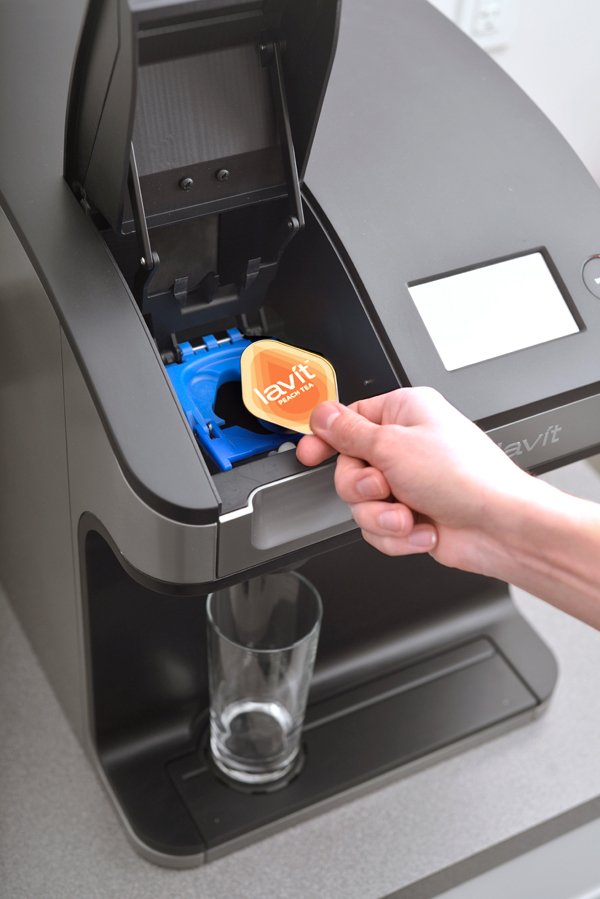 A person inserting a Lavit pod into a portable beverage dispenser machine.